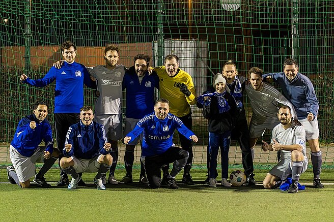 Das Bild stellt wahrscheinlich eine Fußballmannschaft oder eine gemeinsame Sportgruppe dar, die nach einem Spiel oder Training ein Erinnerungsfoto macht.