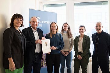 Personengruppe steht gemeinsam in einem Raum, hält ein Dokument und posiert vor einem Banner für ein offizielles Foto. Foto: Generalstaatsanwaltschaft Berlin