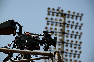 TV camera on a platform, in the background blurred floodlights of a stadium against a blue sky. Photo: Sandra Ritschel
