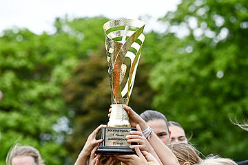 Mehrere Hände heben einen Pokal in die Höhe. Im Hintergrund sind Bäume.