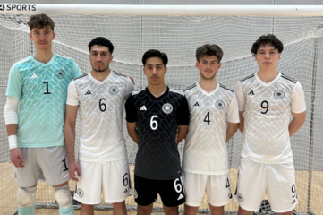 Fünf Personen stehen nebeneinander vor einem Hallentor. Alle tragen Sporttrikots. Vier Personen tragen helle Trikots mit schwarzen Nummern, eine Person in der Mitte trägt ein schwarzes Trikot. Auf den Trikots sind die Nummern 1, 6, 6, 4 und 9 zu sehen. Die Personen stehen aufrecht und schauen nach vorne.