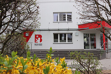 Ein Verbandsgebäude mit weiß-roter Fassade und BFV‑Logo, davor Büsche mit gelben Blüten; Fenster und Eingang liegen ruhig an einer Straße. Foto: BFV