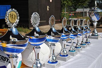 Mehrere glänzende Pokale und Bälle stehen auf einem Tisch – bereit für eine faire und offene Siegerehrung.