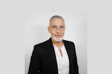 A person with gray hair wears a black jacket and white shirt against a light background. Photo: Dirk Zimmermann