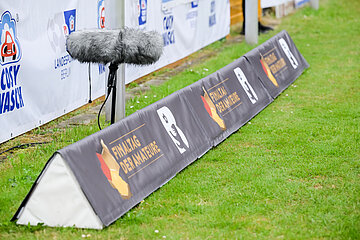A long advertising banner stands on the grass at the edge of the pitch; next to it is a microphone with a windscreen, backed by other sponsor areas. Photo: Sandra Ritschel