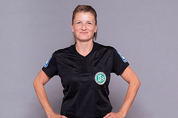 Das Foto zeigt eine Person in einem schwarzen Schiedsrichtertrikot mit dem Logo des Deutschen Fußball-Bundes (DFB) auf der linken Brustseite. Auf beiden Ärmeln des Trikots sind blaue Abzeichen zu sehen.