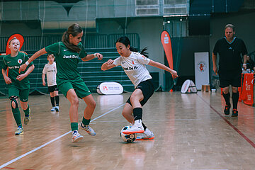 Eine Person in weiß kontrolliert den Ball, während mehrere Personen in grünen Trikots auf dem Hallenboden verteidigen. Foto: Loredana Zafisambondaoky