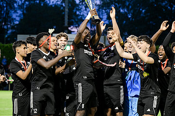 Mehrere Personen in schwarzen Trikots jubeln dicht zusammen, eine Person hält den Pokal hoch, alle tragen Medaillen auf dem Fußballfeld. Foto: Sandra Ritschel