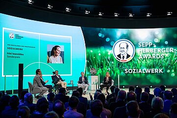 Podiumsdiskussion bei den Sepp-Herberger-Awards mit vier Personen auf Bühne, großem grünen Hintergrund und Publikum im Vordergrund. Foto: Carsten Kobow/DFB-Stiftung Sepp Herberger