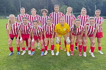Eine Fußballmannschaft in rot-weiß gestreiften Trikots und roten Hosen posiert gemeinsam auf einem grünen Fußballfeld.