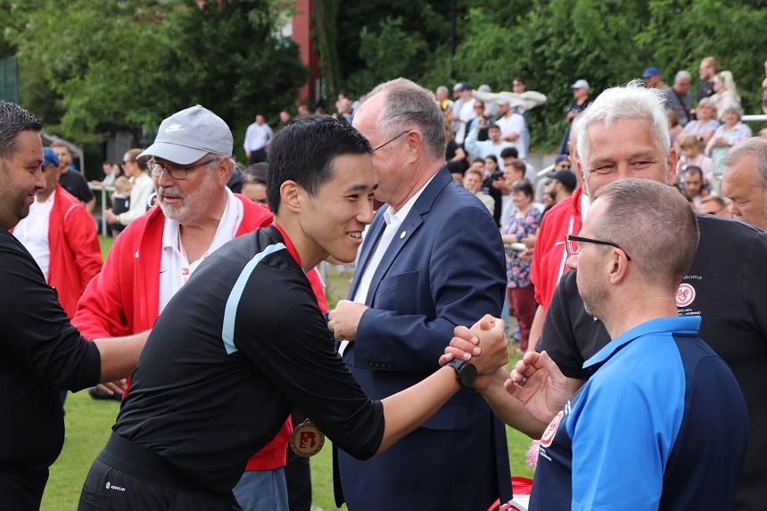 Ein goldener Pokal mit einem rot-weißen Banner, auf dem "Berliner Pokalsieger D-Juniorinnen" steht. Der Pokal steht auf einem Tisch, und im Hintergrund ist ein grünes Feld zu sehen.