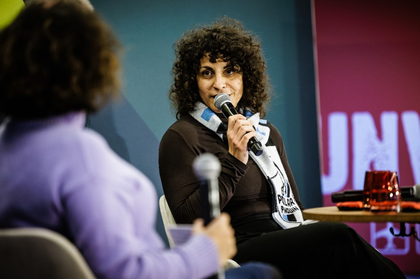 Two people sit in a round table, holding microphones; red glasses and another microphone are on the table. Photo: DFB/Getty Images
