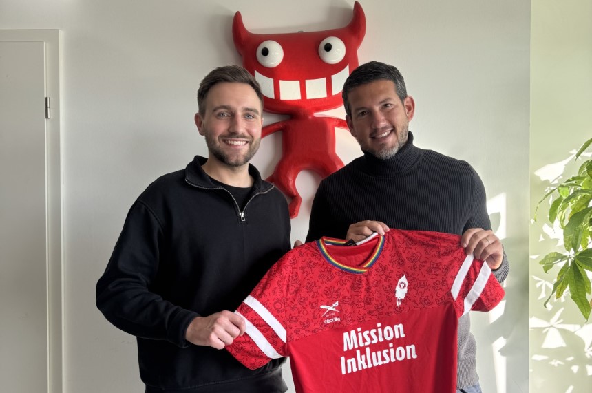 Two people hold a red soccer jersey with the inscription "Mission Inklusion" in front of a wall with a red figure and big eyes. Photo: BFV