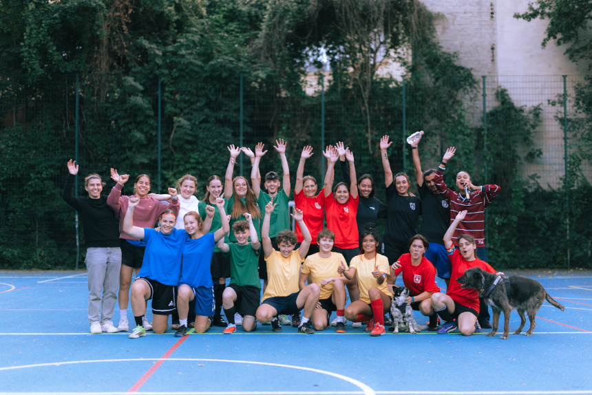 Gruppenfoto auf einem Outdoor-Sportplatz: Viele Personen in bunten Trikots posieren mit erhobenen Armen, zwei Hunde sitzen vorne. Foto: Loredana Zafisambondaoky