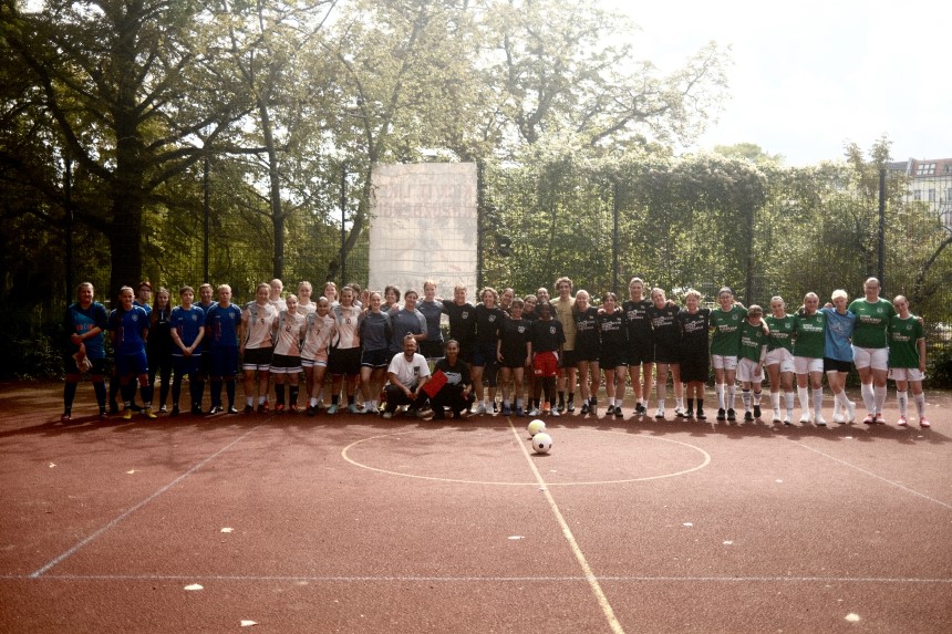 Large group in sportswear on a red square, surrounded by trees and a fence. Photo: Lisa Loriene