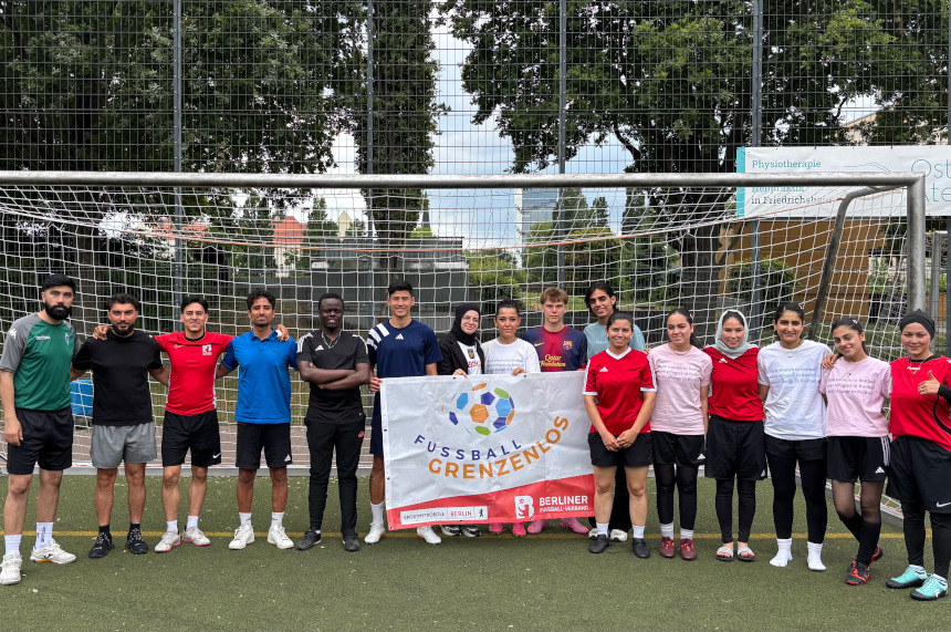 A group of people stands in front of a soccer goal holding a banner that reads “SOCCER KNOWS NO BOUNDARIES”; training gear, a net, and trees are visible in the background. Photo: BFV