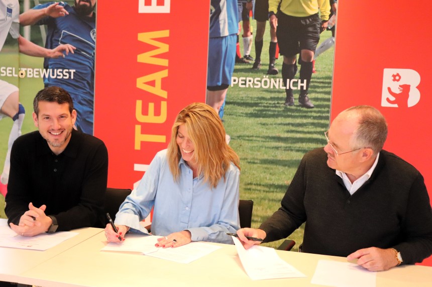 Drei Personen sitzen an einem Tisch und unterschreiben gemeinsam Dokumente vor bunten Sportmotiven. Foto: BFV