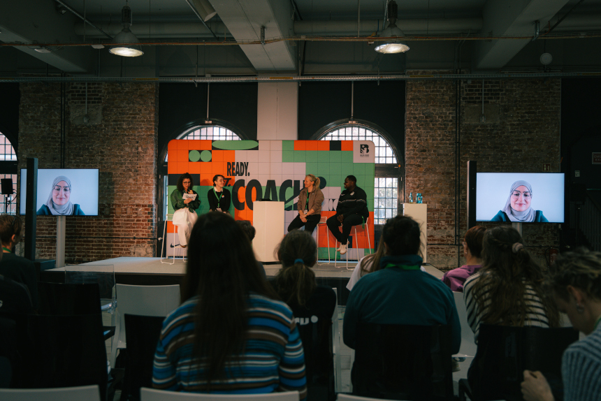Panel discussion in large hall; several people sit on stage, audience listens, two screens flank the scene. Photo: Loredana Zafisambondaoky