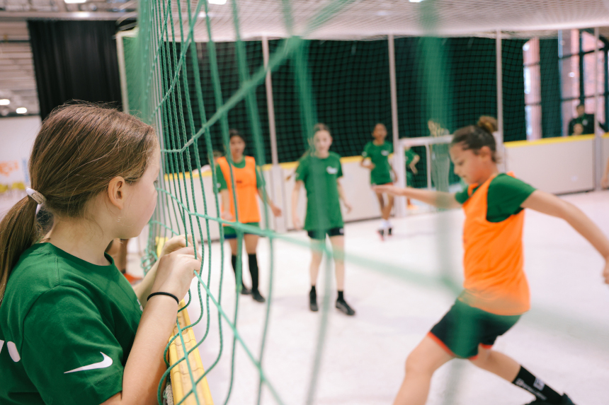 Children play soccer in a hall; some practise on the net, others actively move around the pitch. Photo: Lea Gleisberg