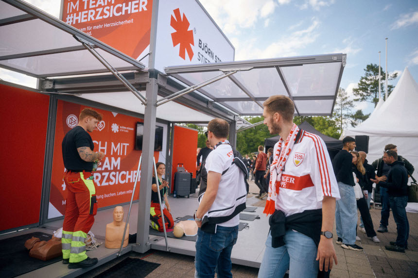 Several people stand at an information stand on heart safety, look at training dummies and get into conversation on a busy event site. Photo: Lennart Ritscher/Björn Steiger Foundation