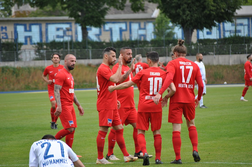 Das Foto zeigt eine Szene auf einem Fußballfeld. Mehrere Spieler sind zu sehen, die sich offenbar mitten im Spiel oder in einer Spielpause befinden. Die meisten Spieler tragen rote Trikots mit dem Schriftzug „Hertha BSC“ auf dem Rücken.