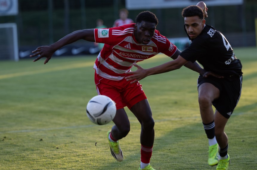 Zwei Spielende in roten und schwarzen Trikots sprinten über den Rasen und kämpfen eng um den Ball während einer Spielsituation. Foto: Martin Böhrer/BFV