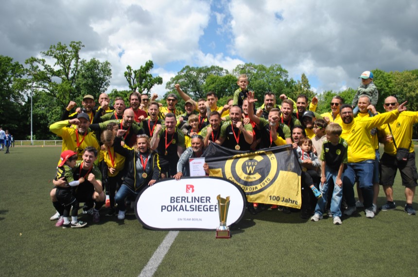 Eine Fußballmannschaft feiert mit Medaillen, Pokal und einem Schild mit der Aufschrift „Berliner Pokalsieger“. Foto: BFV