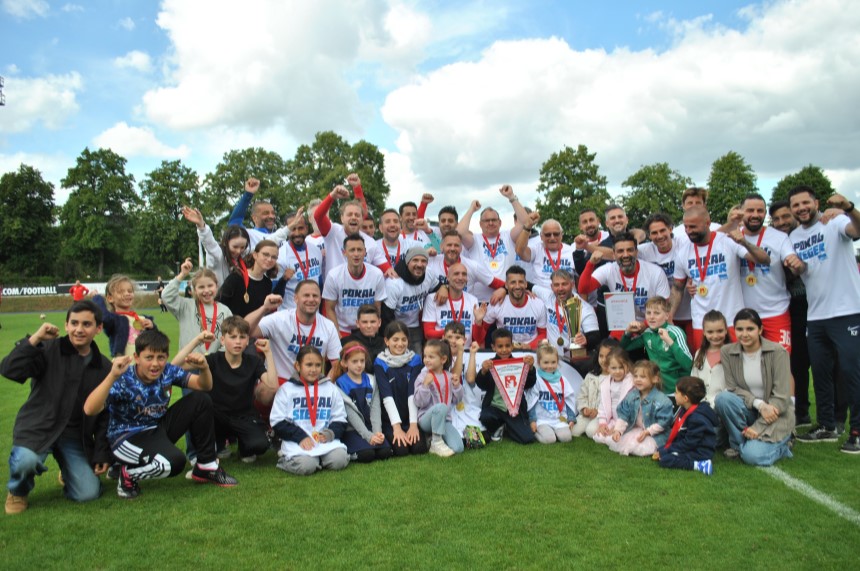 Eine große Gruppe aus Erwachsenen und Kindern posiert auf einem Fußballfeld mit Medaillen und einem Pokal. Foto: BFV