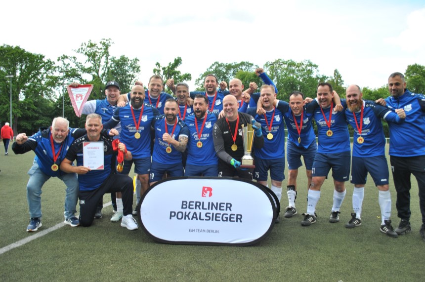 Eine Fußballmannschaft in blauen Trikots feiert auf dem Fußballplatz mit Medaillen und Pokal den Gewinn des Berliner Pokals. Foto: BFV