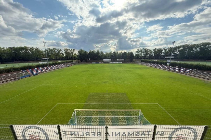 Grüner Fußballplatz mit leeren Tribünen unter einem bewölkten Himmel, gesehen frontal hinter einem Tor. Foto: SV Tasmania Berlin