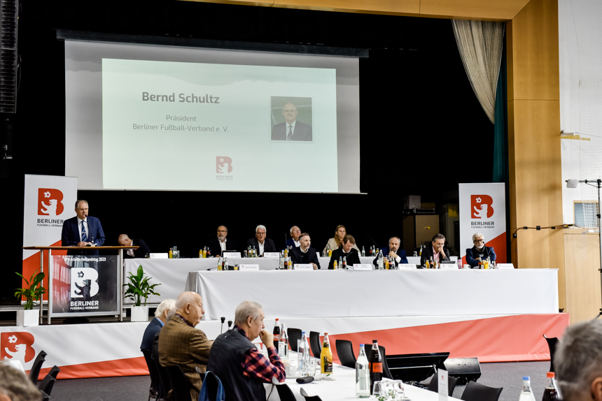 Several people sit at a long table on a stage, in front of the audience; presentation shows "Bernd Schultz, President of the Berlin Football Association". Photo: Sandra Ritschel