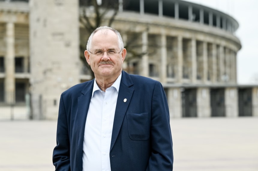 A person in a dark suit stands in front of the historic Olympic Stadium in Berlin, with columns and a round arch in the background. Photo: Sandra Ritschel