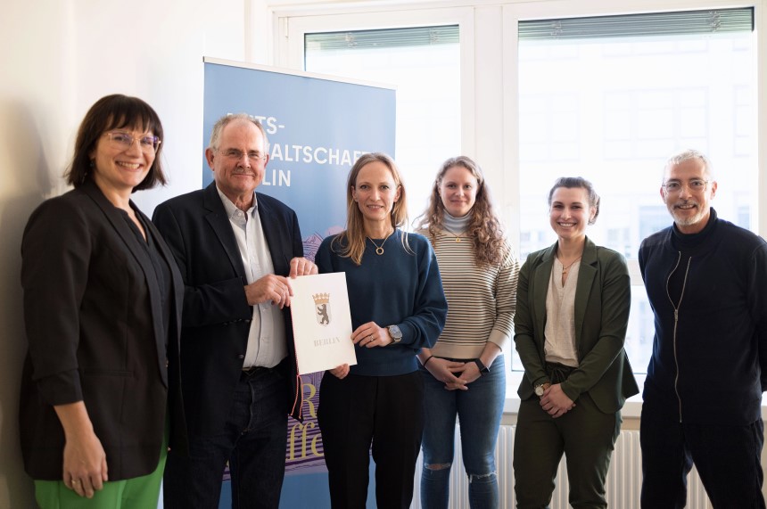 Personengruppe steht gemeinsam in einem Raum, hält ein Dokument und posiert vor einem Banner für ein offizielles Foto. Foto: Generalstaatsanwaltschaft Berlin