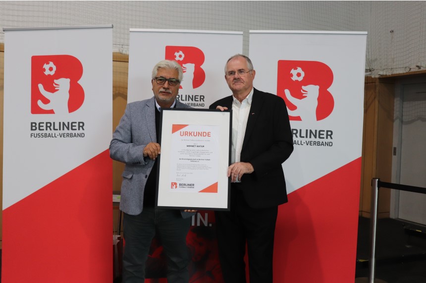 Two people hold a large certificate in front of two roll-ups with the logo of the Berlin Football Association. Photo: BFV