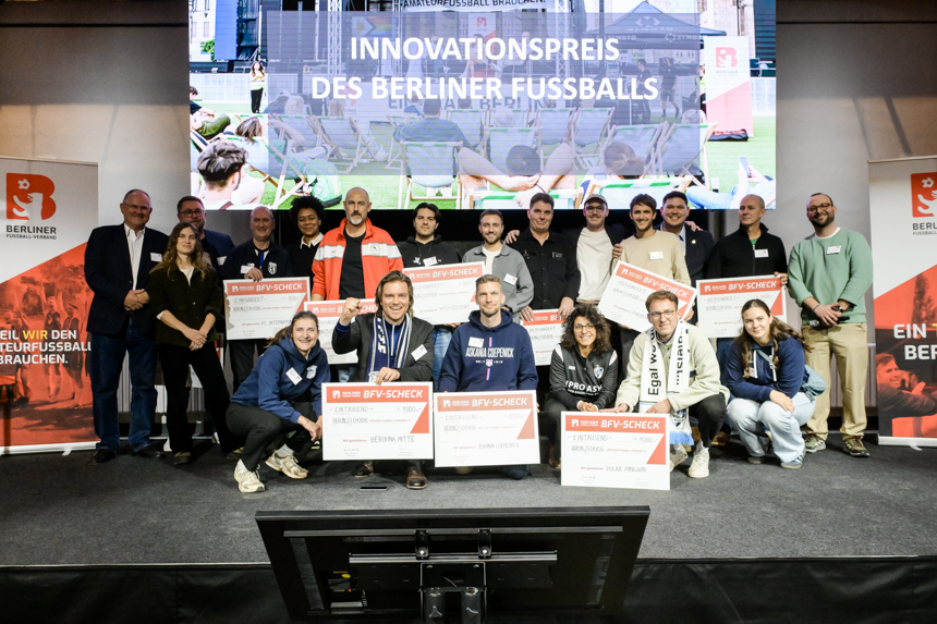 Große Gruppe auf einer Bühne hält Gutscheinschecks und feiert den Innovationspreis des Berliner Fußballs vor einer Leinwand und Bannern. Foto: Sandra Ritschel