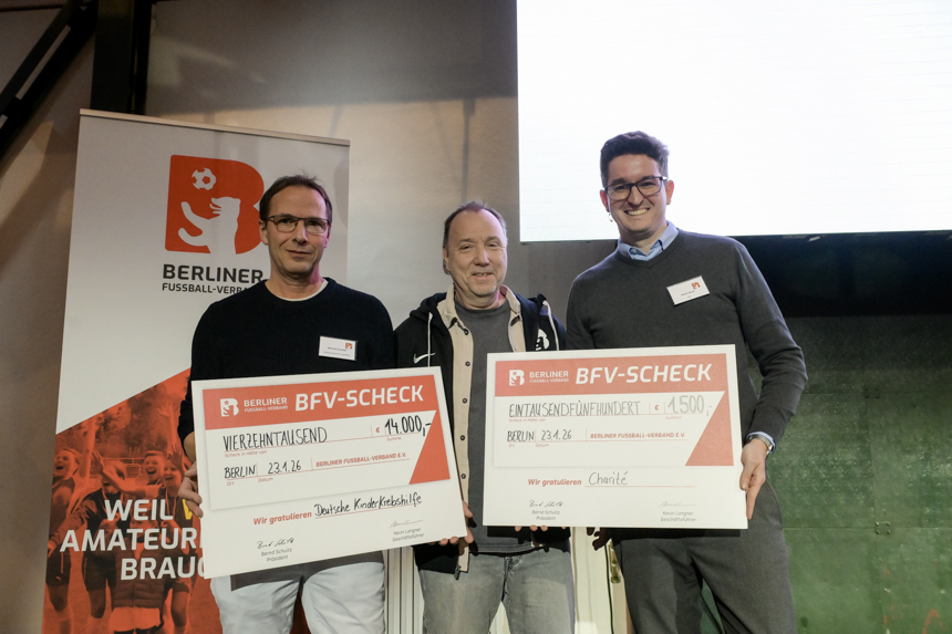 Drei Personen stehen vor einem Banner des Berliner Fußball-Verbands und halten zwei große Spendenschecks in die Kamera. Foto: Sandra Ritschel