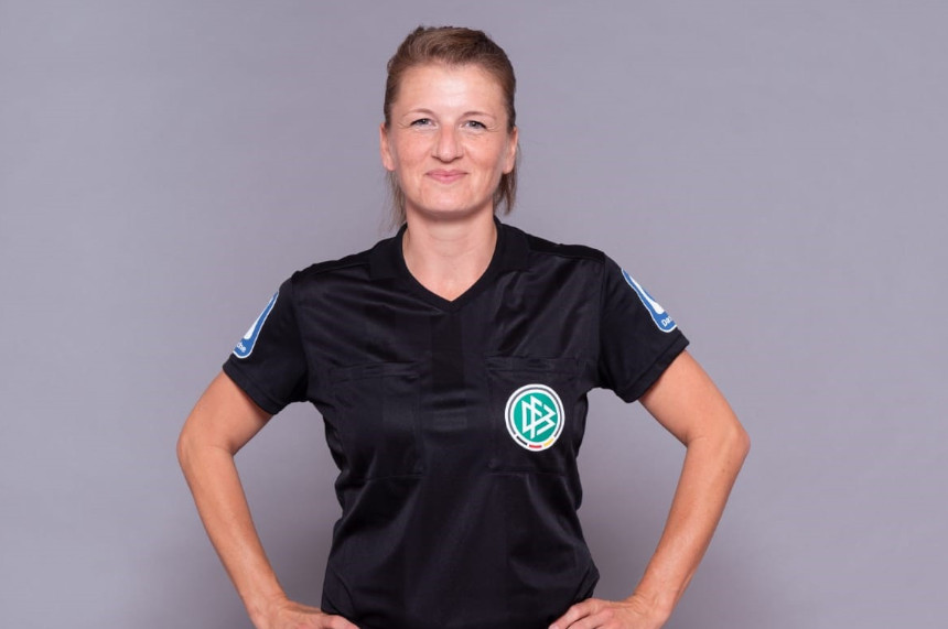 Das Foto zeigt eine Person in einem schwarzen Schiedsrichtertrikot mit dem Logo des Deutschen Fußball-Bundes (DFB) auf der linken Brustseite. Auf beiden Ärmeln des Trikots sind blaue Abzeichen zu sehen.