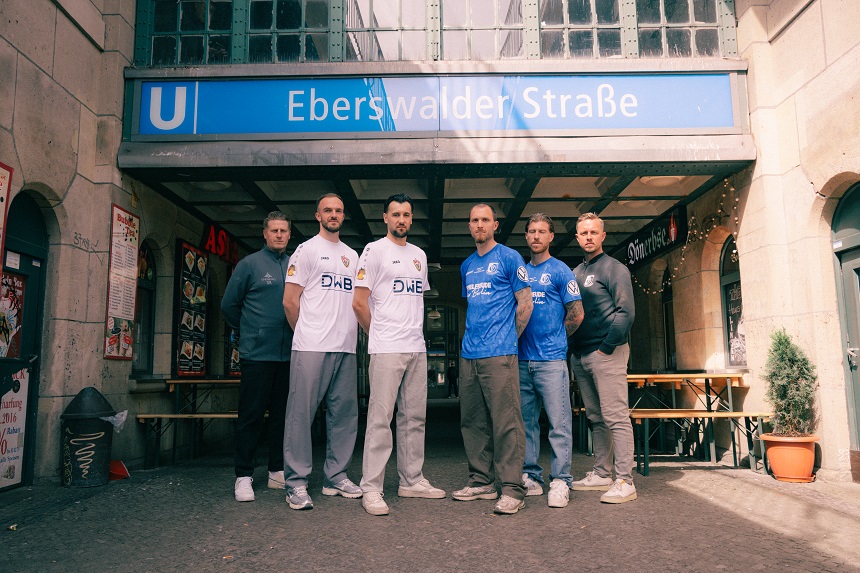 Six people stand in front of the entrance to Eberswalder Straße subway station and pose for a group photo. Some are wearing soccer shirts, others casual clothes.