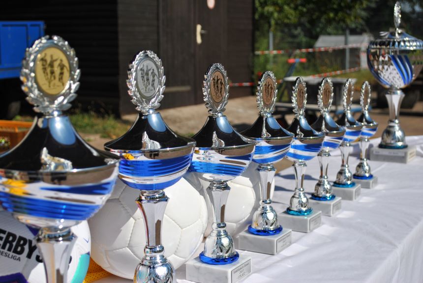 Mehrere glänzende Pokale und Bälle stehen auf einem Tisch – bereit für eine faire und offene Siegerehrung.