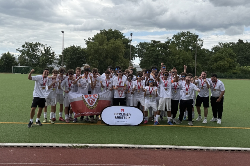 A youth soccer team in white jerseys, wearing medals and holding the club flag and pennants on the soccer field; a group photo taken after winning the Berlin championship.