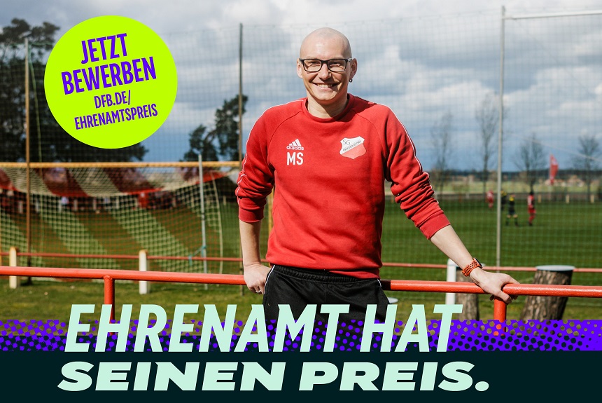 Auf dem Bild steht ein lächelnder Mann auf einem Fußballplatz. Er trägt eine rote Trainingsjacke mit dem Aufdruck „MS“ sowie ein Vereinslogo. Im Hintergrund sind ein Fußballfeld, Tore und einige spielende Personen zu sehen. Der Mann lehnt mit einer Hand entspannt an einem rot‑orangenen Geländer. Links oben befindet sich ein großer gelber Kreis mit der Aufschrift: „Jetzt bewerben – dfb.de/ehrenamtspreis“. Unten im Bild steht in großen, hellen Buchstaben: „Ehrenamt hat seinen Preis.“ Der Gesamtstil wirkt freundlich und motivierend.