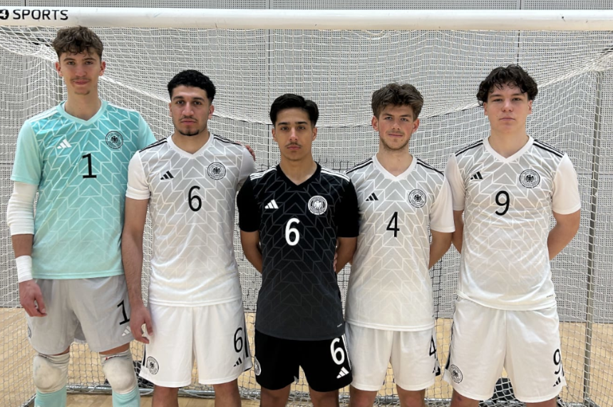 Fünf Personen stehen nebeneinander vor einem Hallentor. Alle tragen Sporttrikots. Vier Personen tragen helle Trikots mit schwarzen Nummern, eine Person in der Mitte trägt ein schwarzes Trikot. Auf den Trikots sind die Nummern 1, 6, 6, 4 und 9 zu sehen. Die Personen stehen aufrecht und schauen nach vorne.