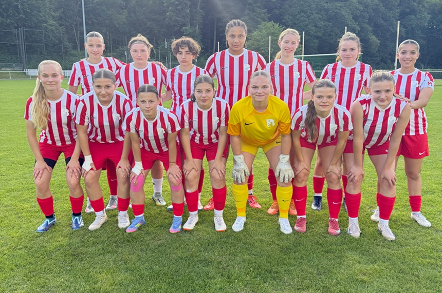 Eine Fußballmannschaft in rot-weiß gestreiften Trikots und roten Hosen posiert gemeinsam auf einem grünen Fußballfeld.