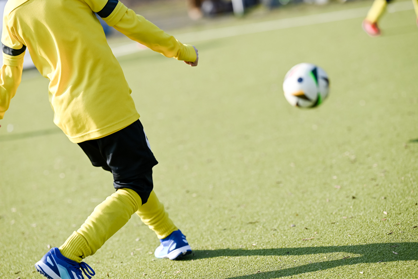 Ein Kind kickt voller Freude einen Ball über das Spielfeld.