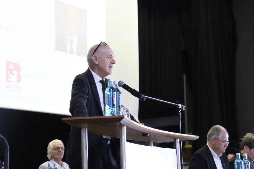 Meeting in a hall: people sitting at round tables, podium with speaker and large screen in front. Photo: BFV
