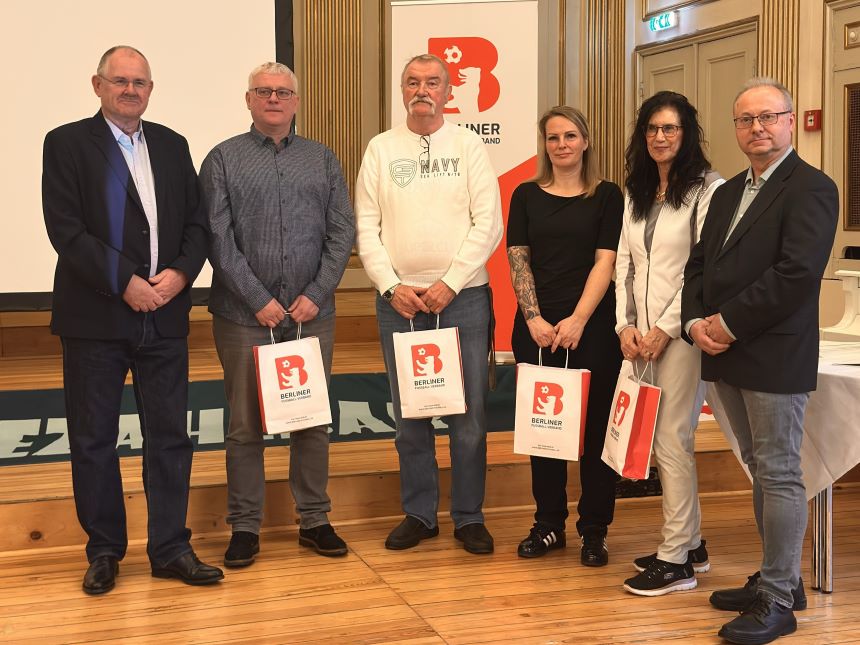 Sechs Menschen stehen in einem Saal, vier halten eine Geschenktüte in der Hand.