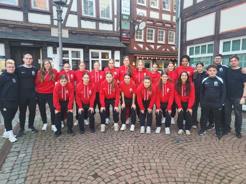 Gruppe in roten Hoodies und dunklen Hosen steht auf einem gepflasterten Platz vor Fachwerkhäusern.