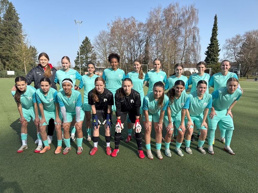 Teamfoto auf dem Fußballplatz: Gruppe in türkisen Trikots und zwei Personen in schwarzer Torwartkleidung vor Bäumen.
